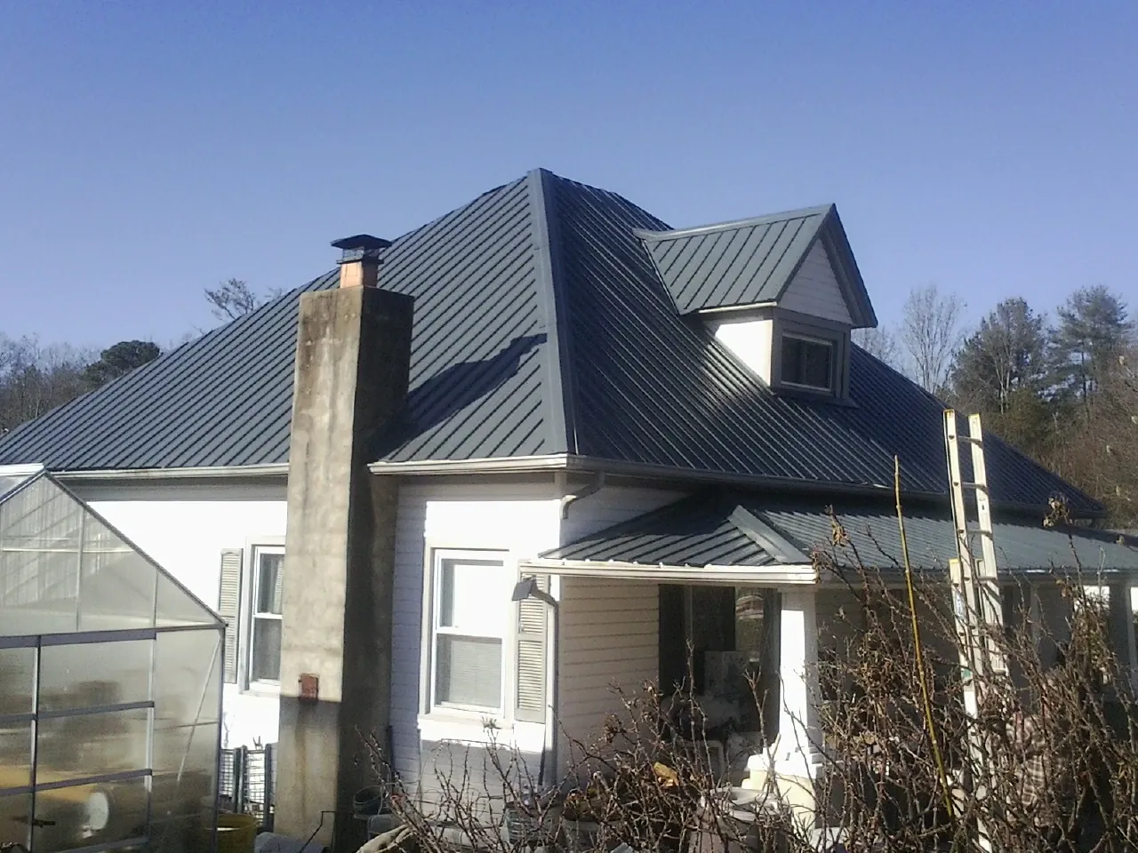 Dark blue standing seam metal roof on a white farmhouse with dormer — Slate & Tile Roof Repair by Roofing Brothers in Whitesboro