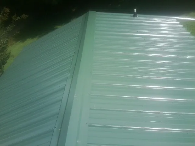 New green metal panels meeting at the ridge of a roof — Flat Roof Repair work by our crew in Whitesboro