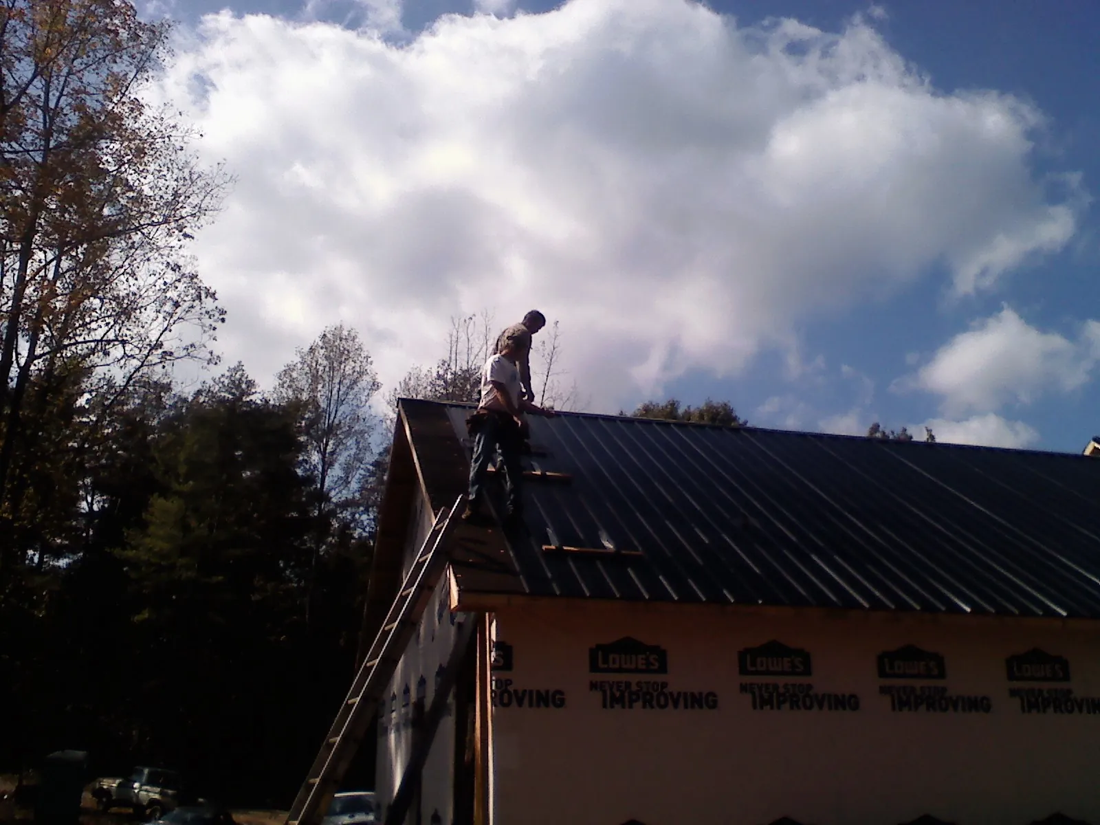 Roofer fastening dark metal panels high against a cloudy sky, from a Roof Inspection job in Whitesboro