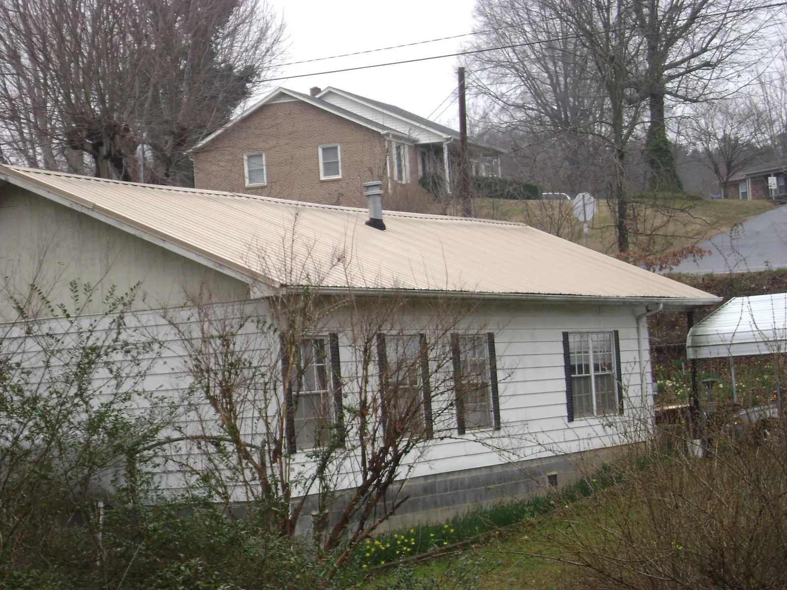 Tan metal roof on a white sided house set into a hillside — Commercial Roofing by Roofing Brothers in Whitesboro