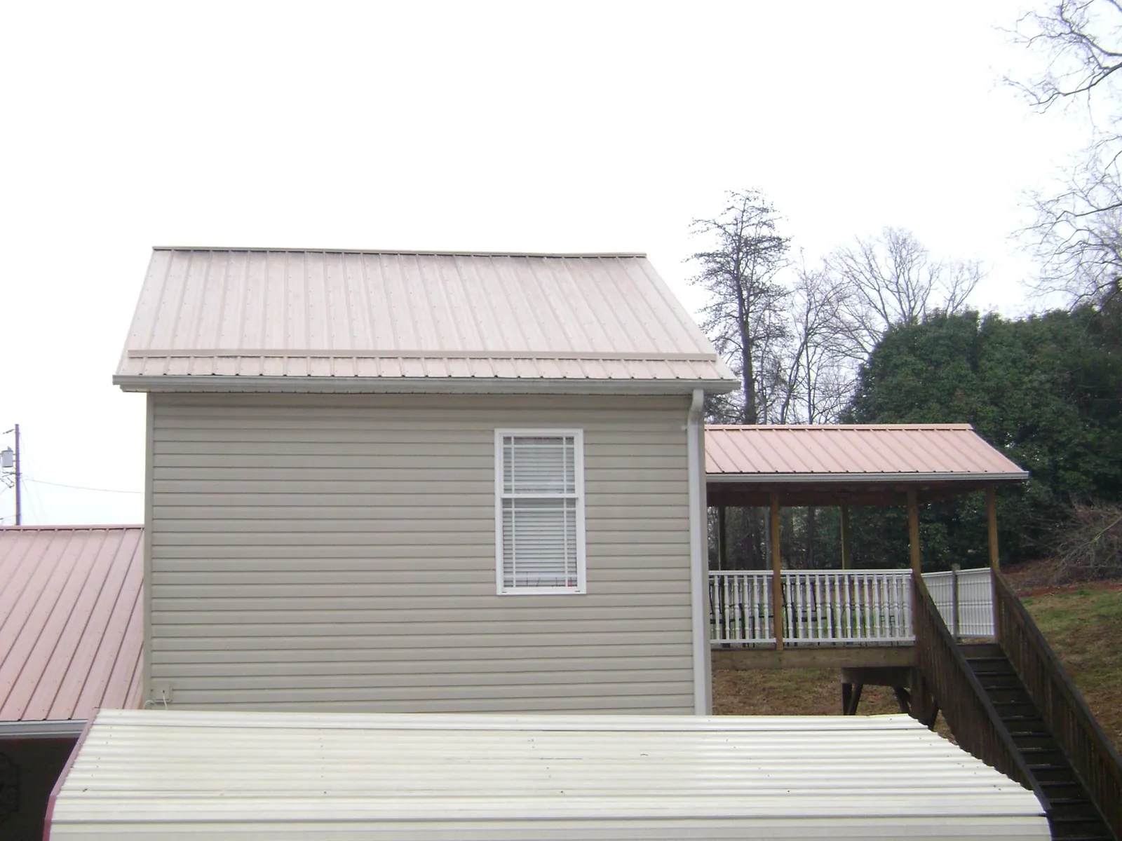 Tan metal roofs on a two story addition and attached porch, from a Roof Replacement job in Whitesboro